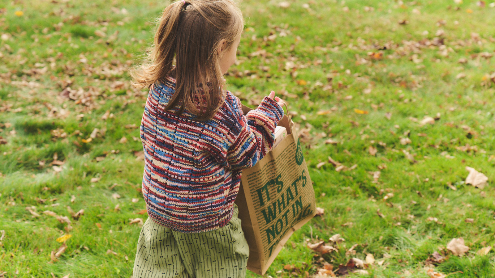 A child carries a bag of household supplies through the yard.