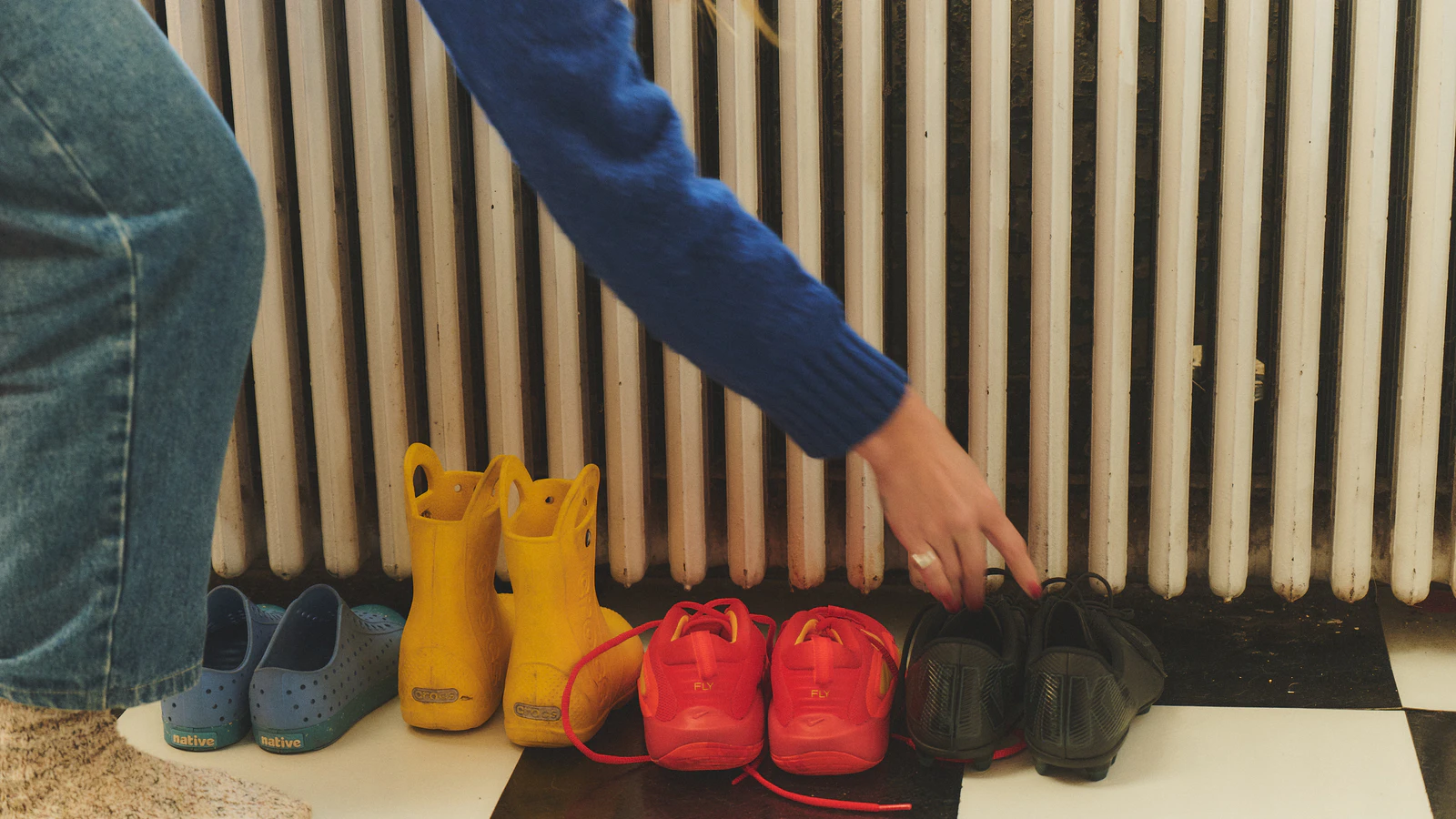 A parent points to a row of children's shoes and boots lined up by the door.