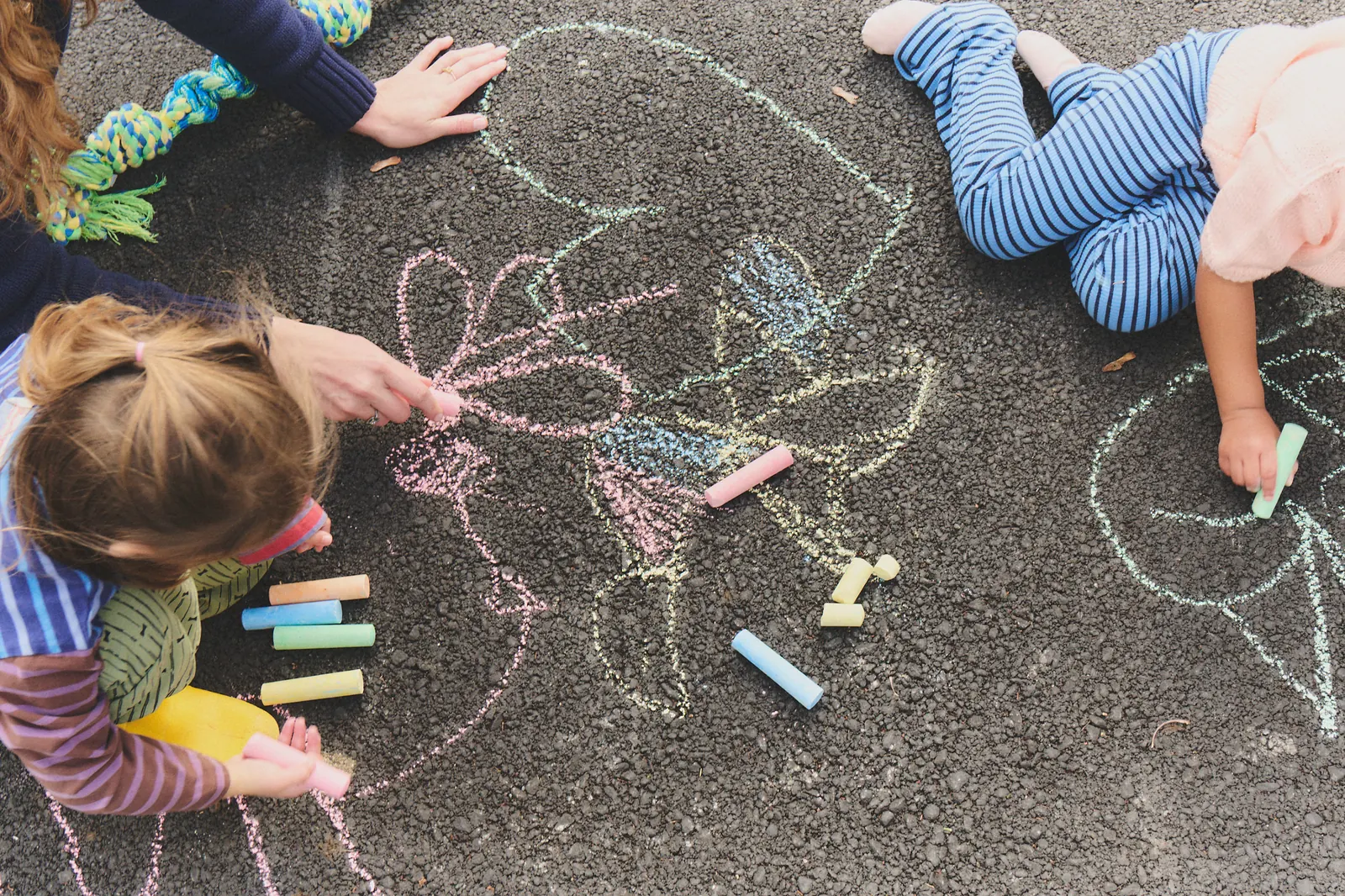 Two children and an adult draw together with sidewalk chalk.