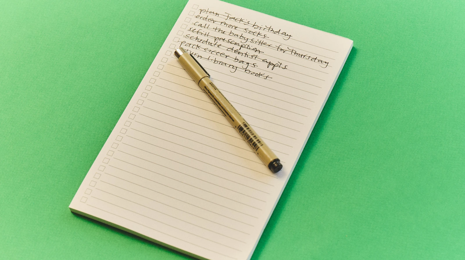A handwritten household to-do list and pen rest on a green tabletop.