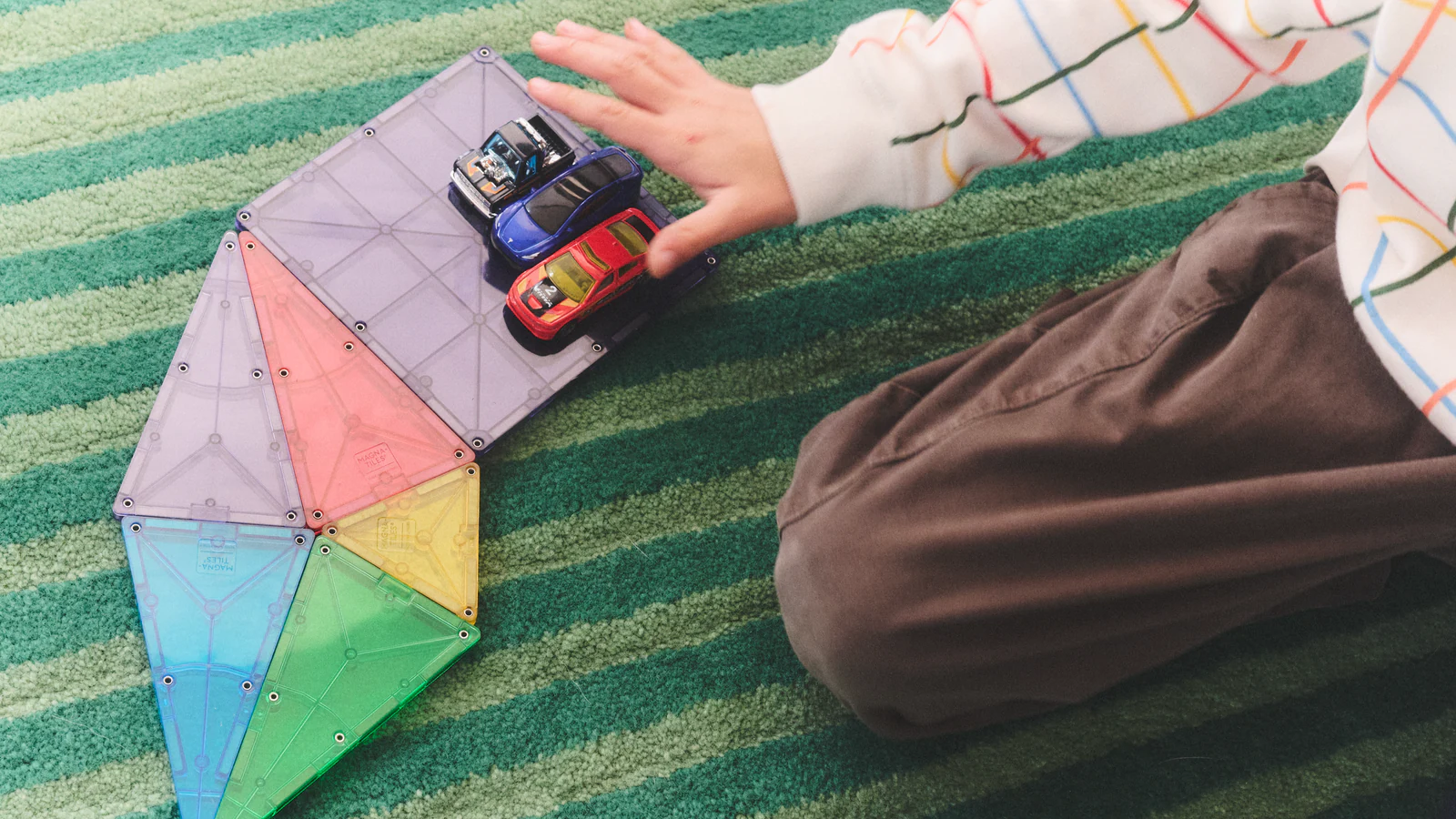 A child brings toy cars together on a magnetic-tile track for a Google Calendar merging guide.