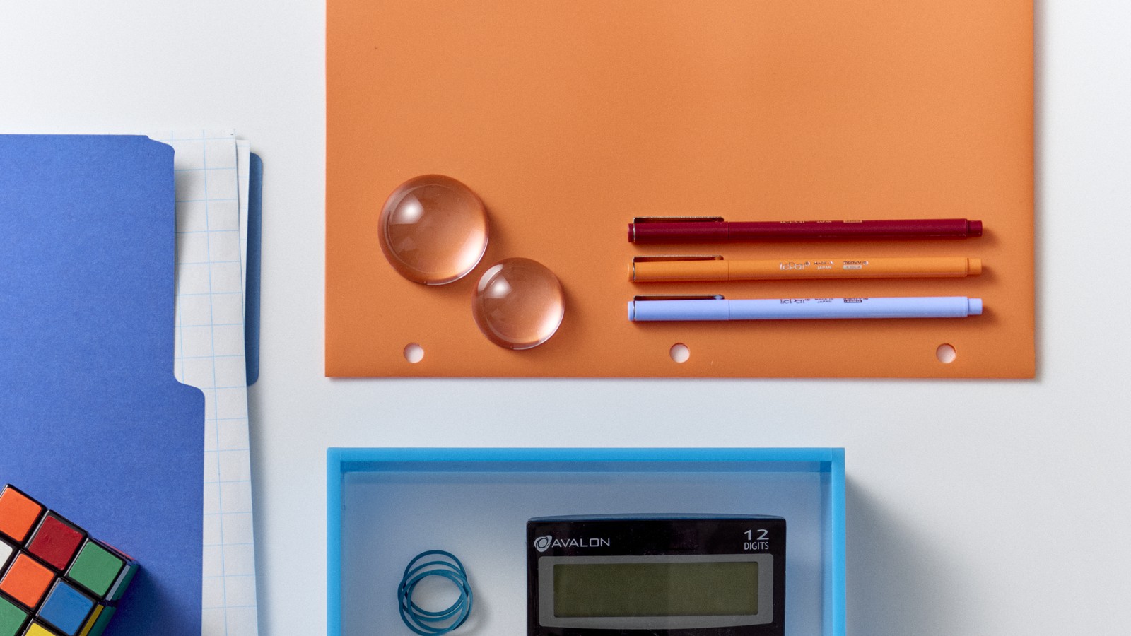 Pens and glass paperweights on orange paper beside a blue folder.
