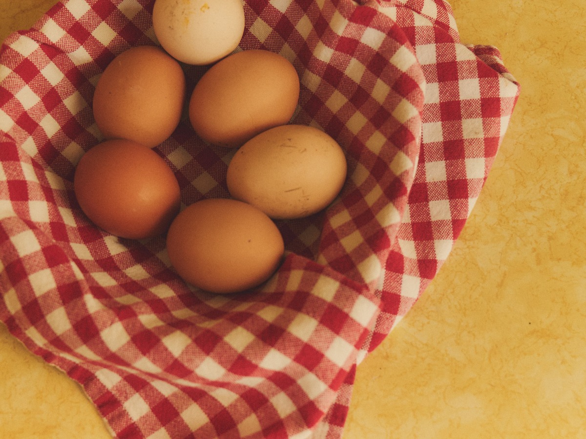 Eggs in a red-and-white gingham-lined basket on a yellow kitchen counter.